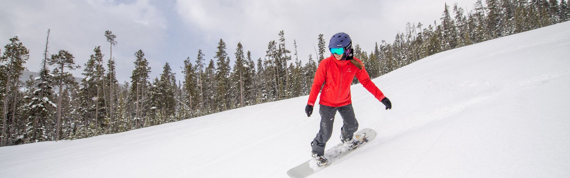 A woman snowboarding in front of trees.